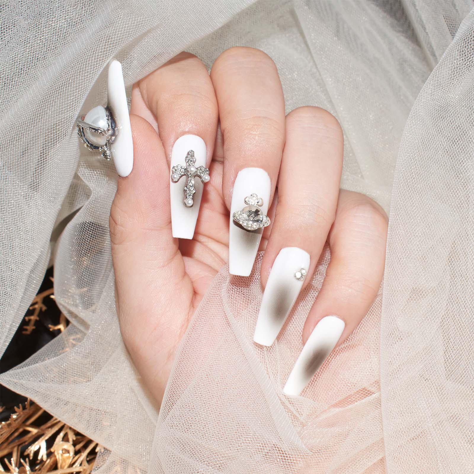 White coffin-shaped press-on nails with 3D crosses, pearls, and rhinestones against a sheer fabric