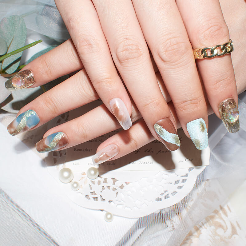 Close-up of hands with Monoschic Blue Gold Mirage Press-On Nails, showcasing an elegant marbled design with blue, brown, and gold tones.