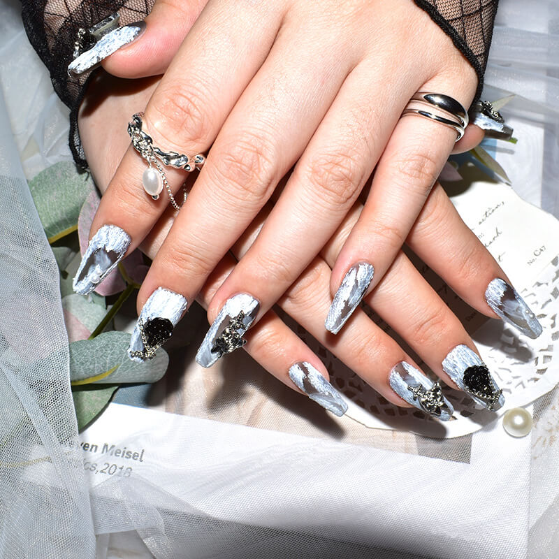 Close-up of hands with Midnight Bloom on White Sands press-on nails featuring white and black design with 3D floral and chain accents.